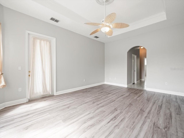 empty room featuring light wood finished floors, visible vents, arched walkways, and a tray ceiling