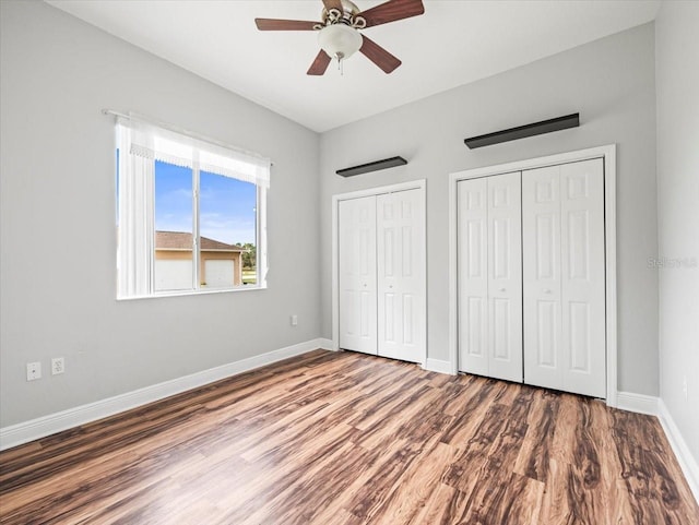 unfurnished bedroom with ceiling fan, wood finished floors, two closets, and baseboards