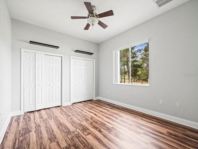 unfurnished bedroom featuring baseboards, visible vents, ceiling fan, wood finished floors, and two closets