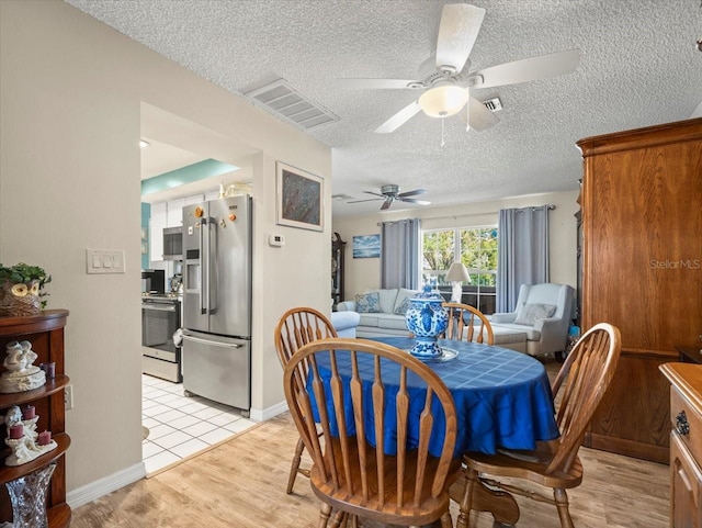 dining space with light wood-style floors, visible vents, ceiling fan, and a textured ceiling