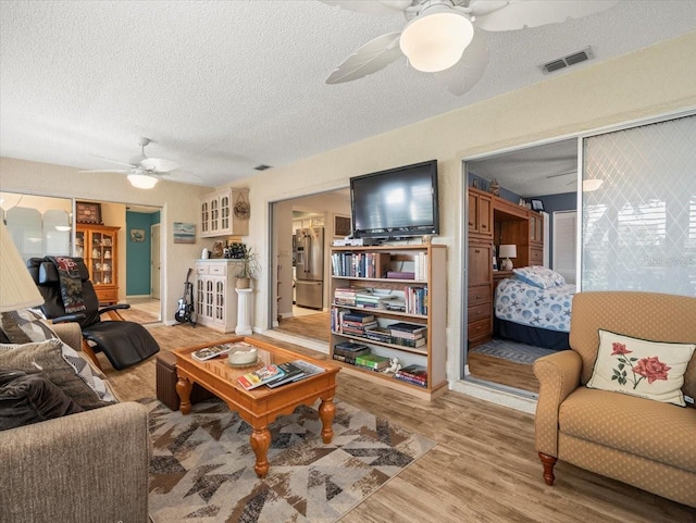 living room featuring a ceiling fan, a textured ceiling, visible vents, and wood finished floors