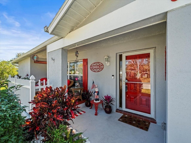 view of exterior entry with fence and stucco siding