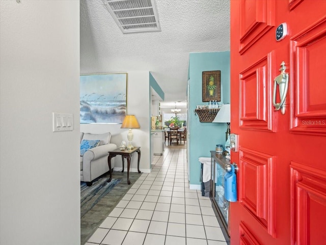 entryway featuring light tile patterned floors, visible vents, a textured ceiling, a chandelier, and baseboards