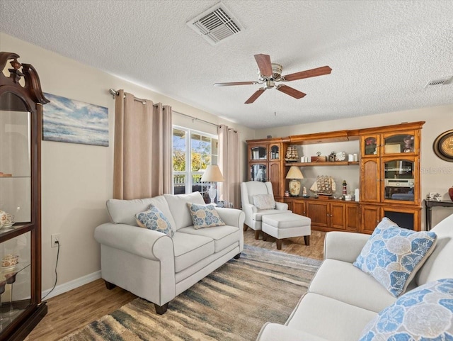 living area with a textured ceiling, light wood finished floors, visible vents, and a ceiling fan