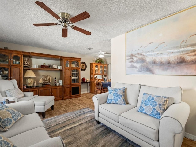 living area featuring a textured ceiling, visible vents, light wood-type flooring, and a ceiling fan