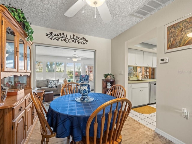 dining room with baseboards, visible vents, light wood-style flooring, ceiling fan, and a textured ceiling