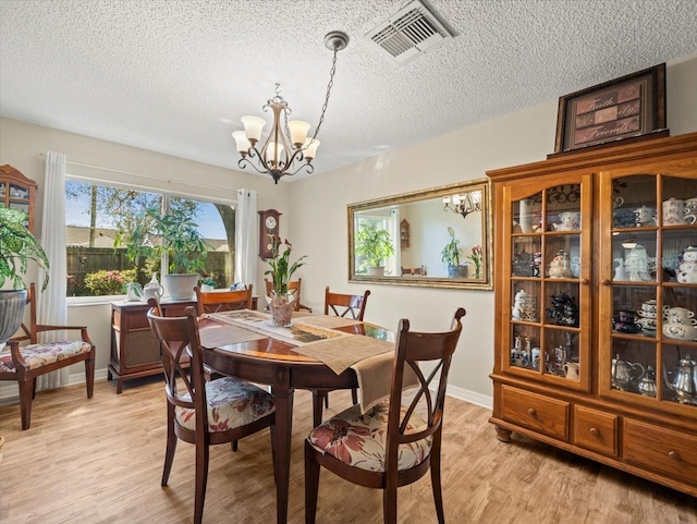 dining room with light wood-style floors, visible vents, a textured ceiling, and an inviting chandelier