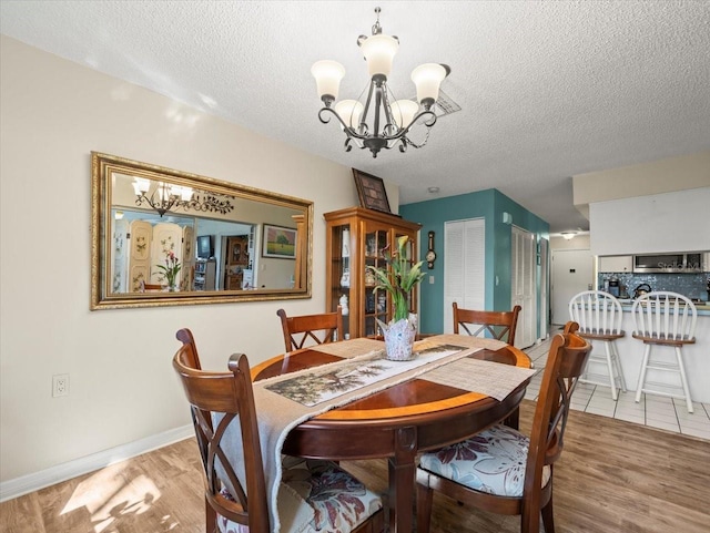 dining area with a textured ceiling, baseboards, light wood-style flooring, and an inviting chandelier