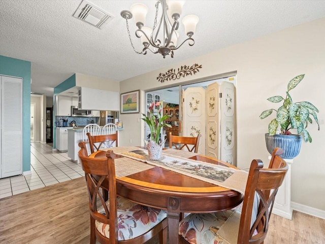 dining space with light wood-type flooring, an inviting chandelier, visible vents, and a textured ceiling