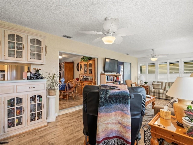 living area with a textured ceiling, a ceiling fan, visible vents, and light wood-style floors