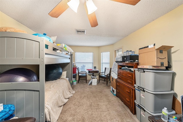 bedroom with a ceiling fan, visible vents, a textured ceiling, and light colored carpet