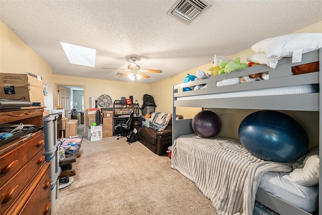 bedroom with a skylight, visible vents, a ceiling fan, light carpet, and a textured ceiling