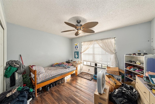 bedroom with a textured ceiling, ceiling fan, and dark wood finished floors