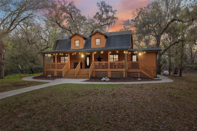 view of front of property featuring faux log siding, stairway, roof with shingles, covered porch, and a front lawn