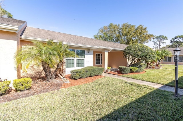 view of front of home featuring stucco siding, a shingled roof, and a front yard