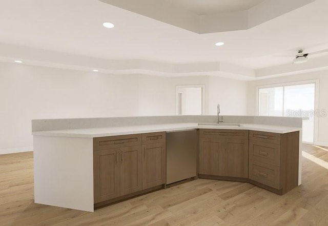 kitchen featuring a tray ceiling, light countertops, a sink, light wood-type flooring, and dishwasher