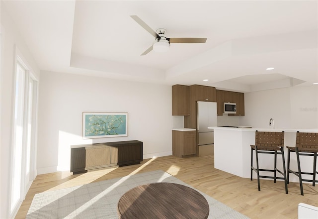 kitchen with a tray ceiling, light wood finished floors, light countertops, freestanding refrigerator, and baseboards