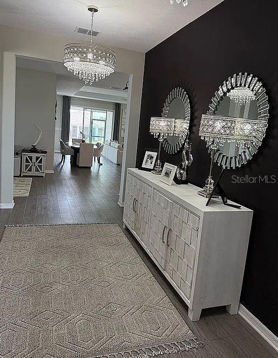 hallway with baseboards, visible vents, wood finished floors, a textured ceiling, and a notable chandelier