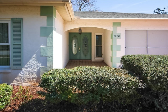 doorway to property with stucco siding and roof with shingles