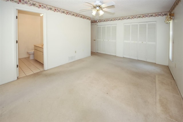 unfurnished bedroom with light carpet, a textured ceiling, and multiple closets