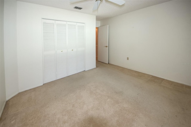 unfurnished bedroom with a closet, light colored carpet, visible vents, a ceiling fan, and a textured ceiling