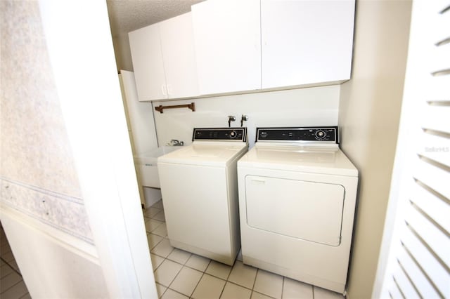 washroom with a textured ceiling, light tile patterned floors, a sink, cabinet space, and washing machine and clothes dryer