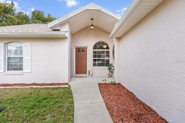 doorway to property featuring a shingled roof, a lawn, and stucco siding