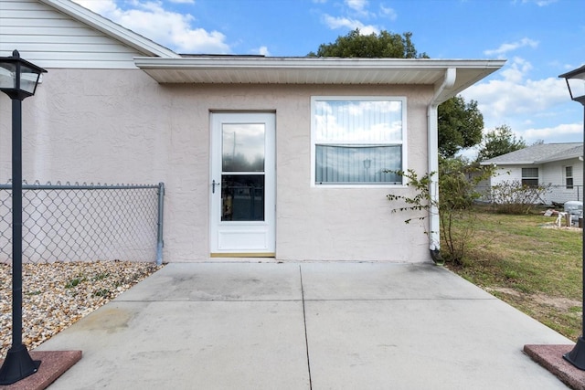 property entrance featuring a patio area, fence, and stucco siding