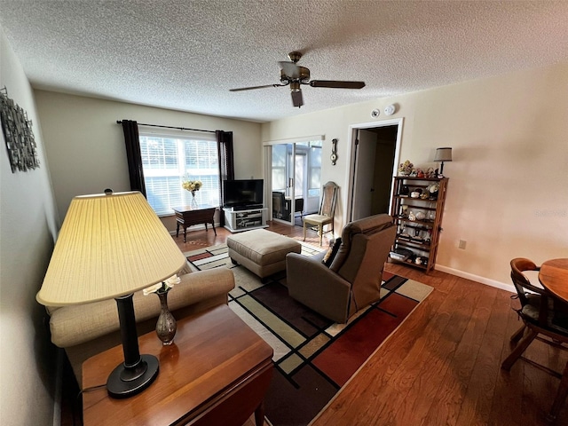 living area featuring a textured ceiling, dark wood-style flooring, a ceiling fan, and baseboards