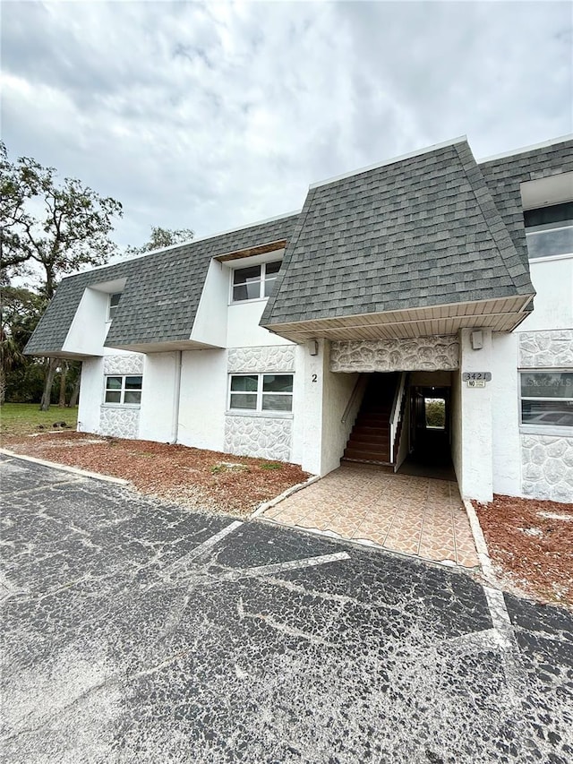 view of home's exterior with a shingled roof, mansard roof, and stucco siding