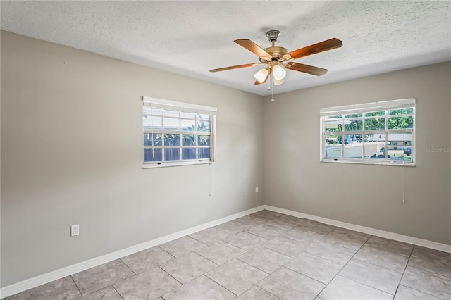 empty room with light tile patterned floors, ceiling fan, baseboards, and a textured ceiling