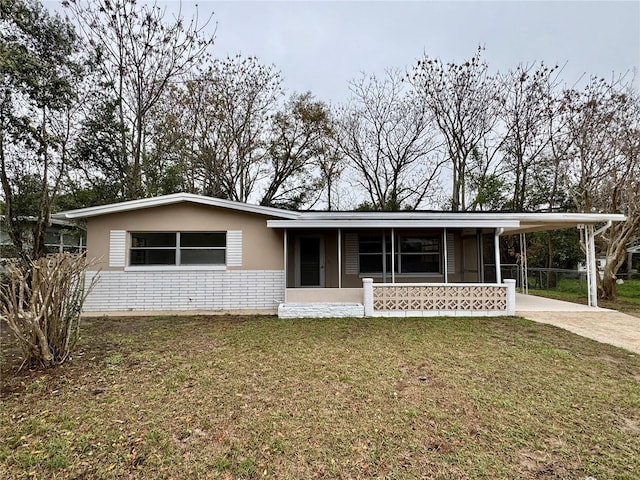 view of front of property featuring driveway, brick siding, a front lawn, a carport, and stucco siding