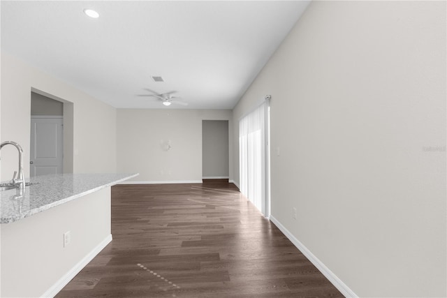 empty room featuring ceiling fan, baseboards, dark wood-type flooring, and a sink