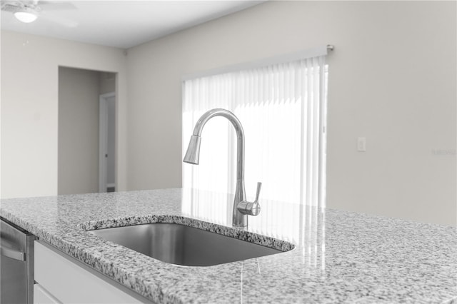 details featuring light stone counters, stainless steel dishwasher, a ceiling fan, white cabinetry, and a sink