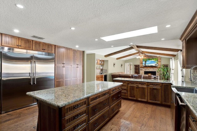 kitchen featuring visible vents, lofted ceiling with skylight, a warm lit fireplace, appliances with stainless steel finishes, and wood finished floors