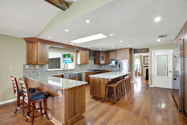 kitchen with a breakfast bar, vaulted ceiling with skylight, stainless steel appliances, wall chimney range hood, and tasteful backsplash