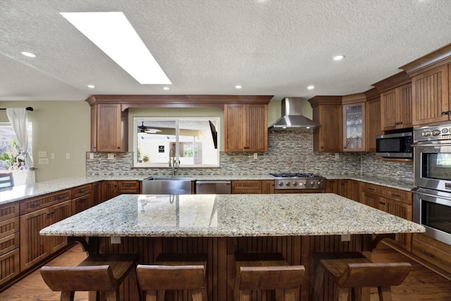 kitchen with a sink, a kitchen island, stainless steel appliances, wall chimney exhaust hood, and decorative backsplash