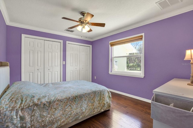 bedroom featuring visible vents, two closets, baseboards, ornamental molding, and dark wood-style flooring