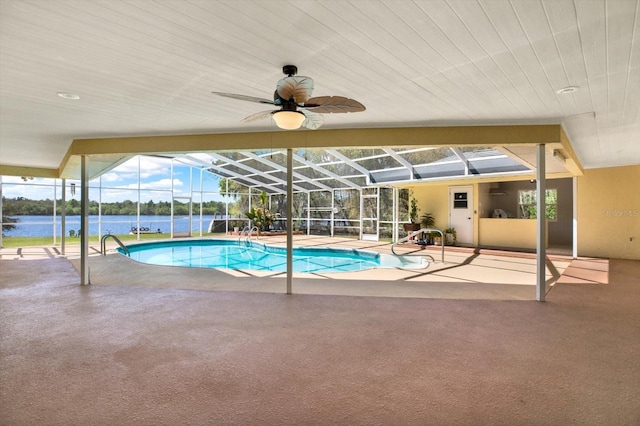 outdoor pool with glass enclosure, a water view, a ceiling fan, and a patio area