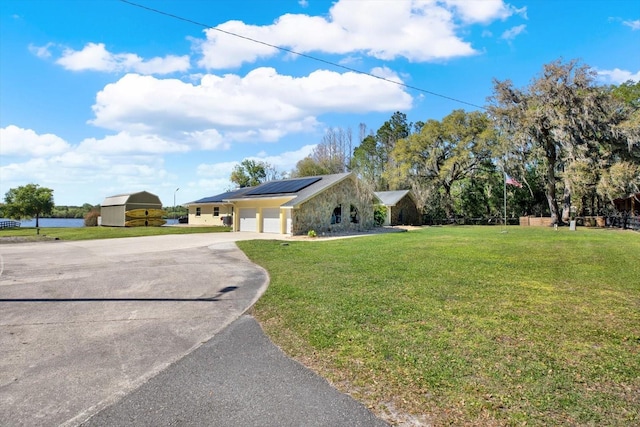 view of property exterior featuring concrete driveway, roof mounted solar panels, a lawn, a garage, and stone siding