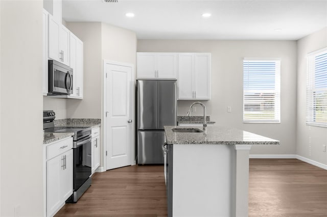 kitchen featuring a center island with sink, white cabinets, light stone counters, appliances with stainless steel finishes, and a sink