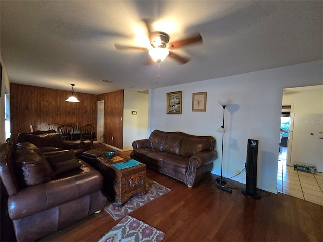 living room featuring a ceiling fan, wooden walls, wood finished floors, and visible vents