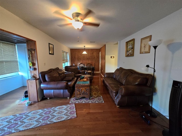 living area with a ceiling fan, wooden walls, and wood finished floors