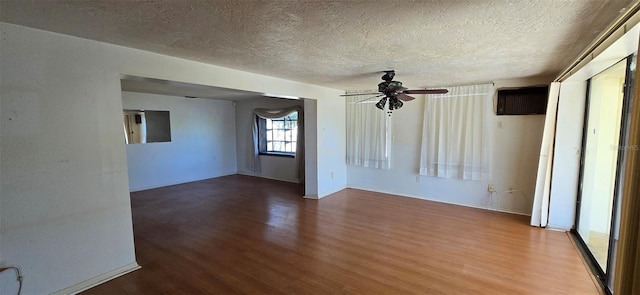 unfurnished room with wood finished floors, a ceiling fan, baseboards, a wall mounted AC, and a textured ceiling