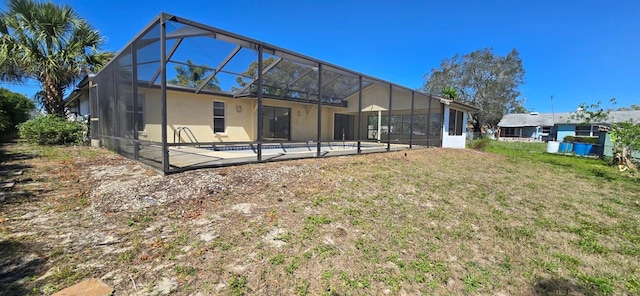 rear view of house with a patio area, stucco siding, a lanai, and a lawn