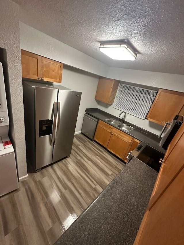 kitchen featuring a sink, appliances with stainless steel finishes, light wood finished floors, brown cabinetry, and dark countertops