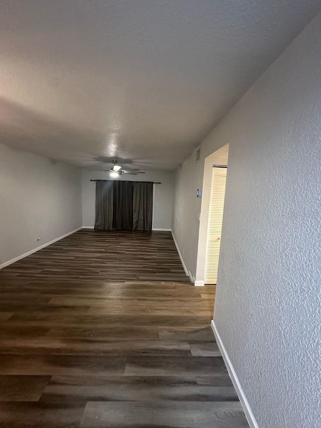 spare room with dark wood-style floors, a textured wall, baseboards, and a ceiling fan