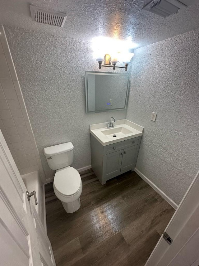 full bathroom featuring visible vents, a textured wall, toilet, wood finished floors, and vanity