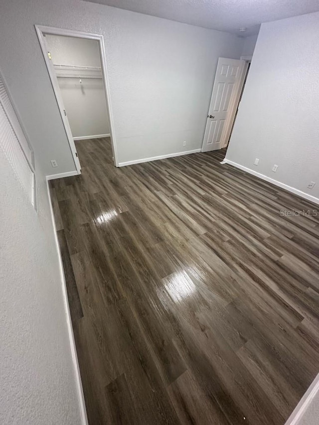 unfurnished bedroom with baseboards, dark wood-type flooring, a walk in closet, a textured ceiling, and a closet