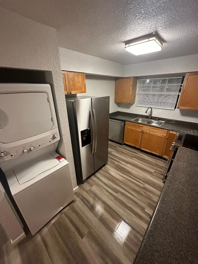 kitchen featuring stacked washer and clothes dryer, dark countertops, appliances with stainless steel finishes, wood finished floors, and a sink